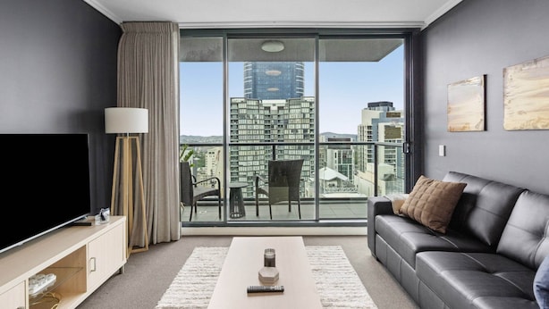 A modern living room with a large window, a flat-screen TV, a sofa, and a coffee table. - Bright 1-bed Retreat in Charlotte Towers (Brisbane)