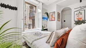A bedroom with a large window, a bed with white and orange bedding, and a view of a balcony. - Romantic cocoon & serenity 8 minutes from the Eiffel Tower (Paris)