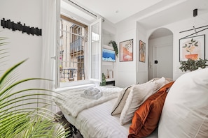 A bedroom with a large window, a bed with white and orange bedding, and a view of a balcony. - Romantic cocoon & serenity 8 minutes from the Eiffel Tower (Paris)