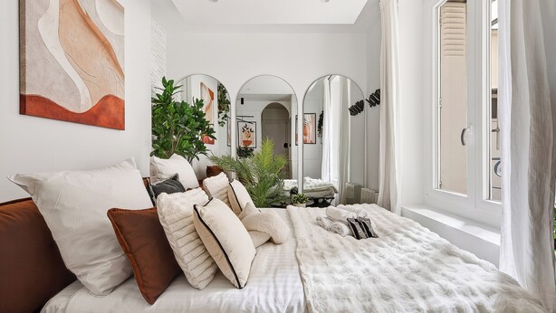 A bedroom with a large bed, multiple pillows, a fluffy white blanket, a large abstract painting, three mirrors, and a potted plant. - Romantic cocoon & serenity 8 minutes from the Eiffel Tower (Paris)