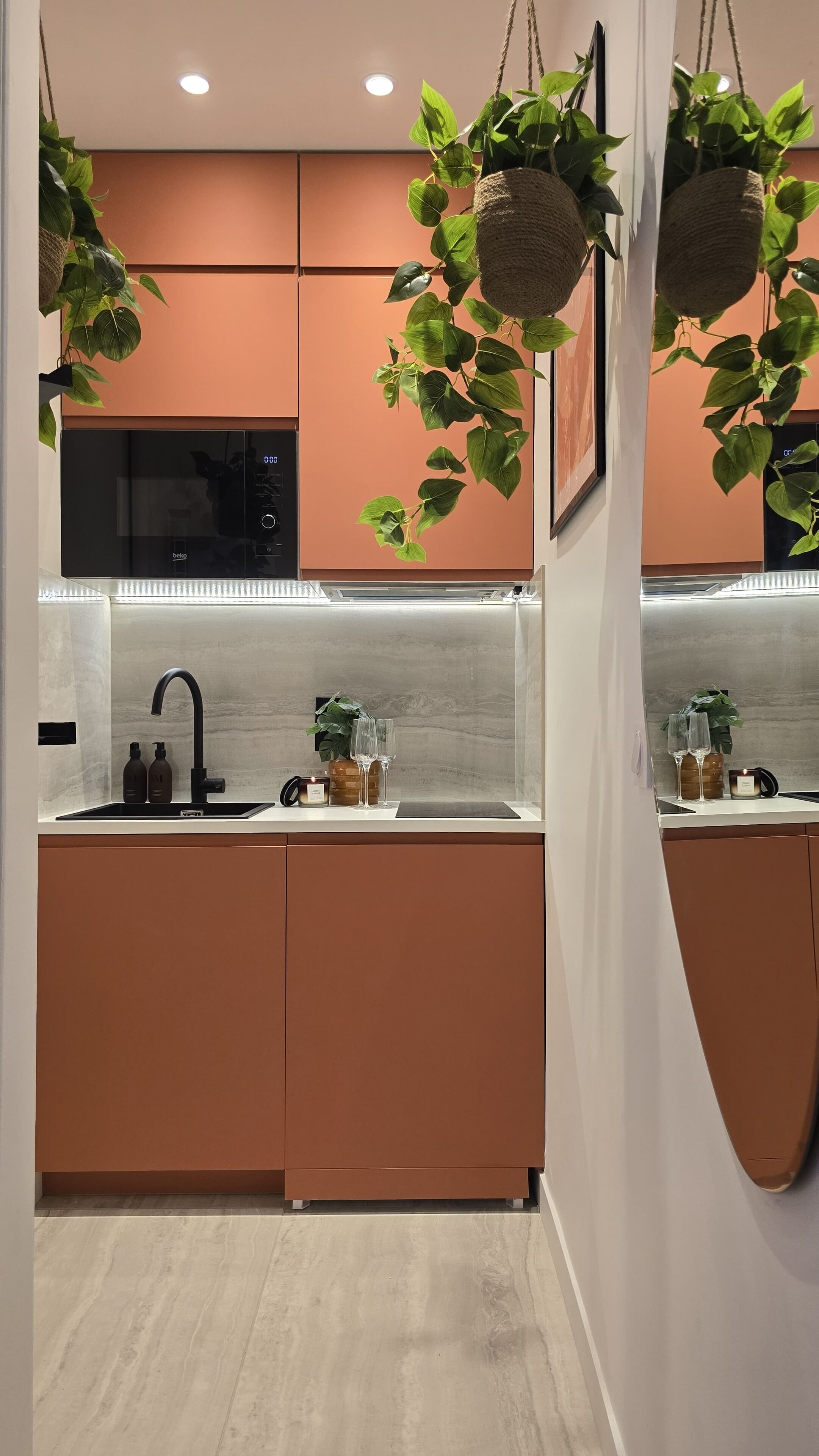 Una cocina moderna con microondas integrado, pileta de acero inoxidable y plantas colgantes.