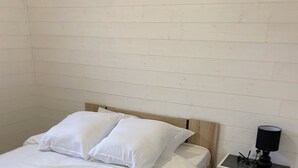 A single bed with white bedding in a room with a white brick wall and a small bedside table with a lamp. - Spacious detached apartment in quiet area (Allouagne)