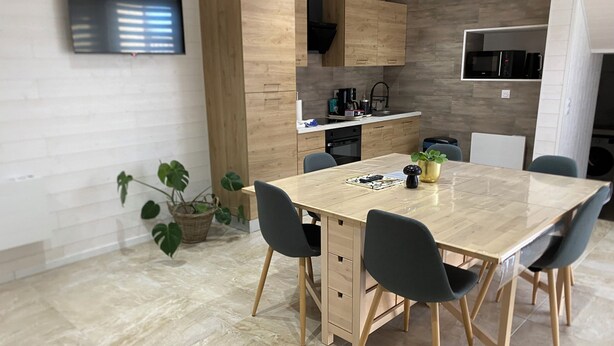 A modern kitchen with wooden cabinets, a built-in microwave, and a dining area with a marble table and chairs. - Spacious detached apartment in quiet area (Allouagne)