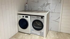 A laundry area with two washing machines, a wooden shelf, a bottle of detergent, and a marble wall. - Spacious detached apartment in quiet area (Allouagne)