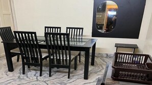 Un coin repas doté d’un sol en marbre, d’une table à manger noire, de six chaises noires, d’un miroir à cadre noir et d’une petite table d’appoint noire sur laquelle se trouve un plateau.