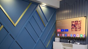 Un salon moderne avec un mur orné d’un motif géométrique bleu, un téléviseur fixé au mur et un meuble de rangement blanc.
