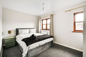 A bedroom with a bed, a nightstand, a lamp, a window with curtains, and a radiator. - Spacious 2 bed house in London - Off street parking and Garden (London)