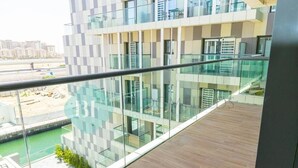 A modern building with a glass facade, a wooden deck, and a view of a green area with construction. - Bloomfields 2BR Duplex Canal View Ra (Abu Dhabi)