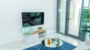 A modern living room with a flat-screen TV, a glass coffee table, and a blue rug. - Bloomfields 2BR Duplex Canal View Ra (Abu Dhabi)