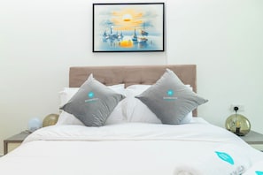 A neatly made bed with two pillows, a framed artwork above it, and a bedside table with a lamp. - Bloomfields 2BR Duplex Canal View Ra (Abu Dhabi)