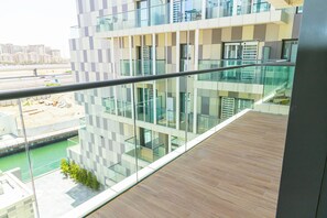 A modern building with a glass facade, a wooden deck, and a view of a construction site. - Bloomfields 2BR Duplex Canal View Ra (Abu Dhabi)