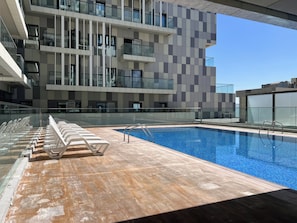 A modern building with a swimming pool, glass railings, and a row of white lounge chairs. - Bloomfields 2BR Duplex Canal View Ra (Abu Dhabi)