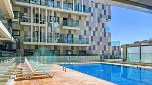 A modern building with a pool area, including a clear pool, lounge chairs, and a glass railing. - Bloomfields 2BR Duplex Canal View Ra (Abu Dhabi)