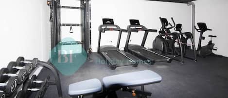 A gym with treadmills, elliptical machines, a bench, and dumbbells.