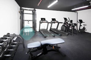 Une salle de sport équipée de tapis de course, de vélos elliptiques, d’un banc de musculation et d’haltères.