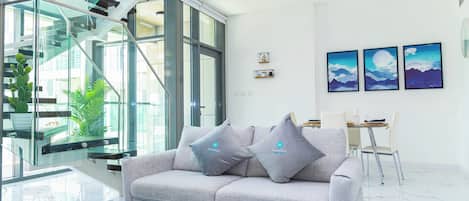 A modern living room with a grey sofa, a glass coffee table, and a staircase with glass railings.