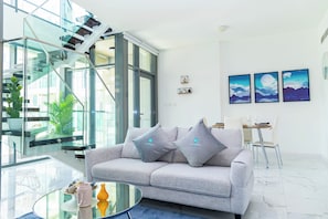 A modern living room with a grey sofa, a glass coffee table, and a staircase with glass railings. - Bloomfields 2BR Duplex Canal View Ra (Abu Dhabi)