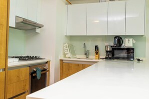 A modern kitchen with white cabinets, a gas stove, a microwave, and a coffee maker. - Bloomfields 2BR Duplex Canal View Ra (Abu Dhabi)