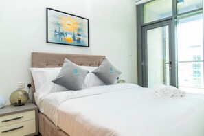 A hotel room with a bed, pillows, a nightstand, a lamp, a framed artwork, and a view through a glass door. - Bloomfields 2BR Duplex Canal View Ra (Abu Dhabi)