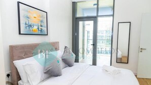A hotel room with a bed, pillows, a painting, a window, and a door. - Bloomfields 2BR Duplex Canal View Ra (Abu Dhabi)