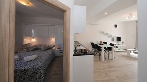 A modern apartment with a kitchenette, dining area, and a bedroom with patterned bedding.