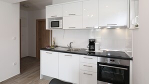 A modern kitchen with white cabinets, a stainless steel sink, a microwave, a coffee maker, and an oven.