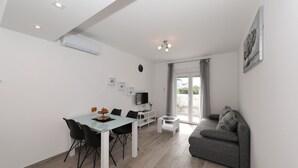 A modern living room with a gray sofa, a dining table with chairs, a TV, and a large window.