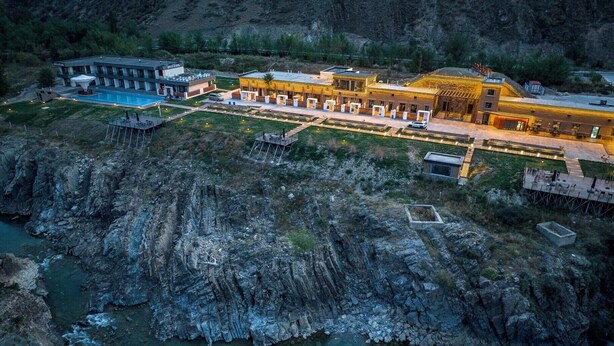 Un hotel con varias construcciones, piscina y un acantilado rocoso.