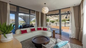 Una sala de estar moderna con un sofá seccional, una mesa de centro redonda y vistas a un paisaje montañoso a través de amplios ventanales.