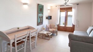 Un salon moderne comprenant un coin repas, un canapé, un fauteuil et une table. Un tableau orne le mur et une fenêtre est agrémentée de rideaux.