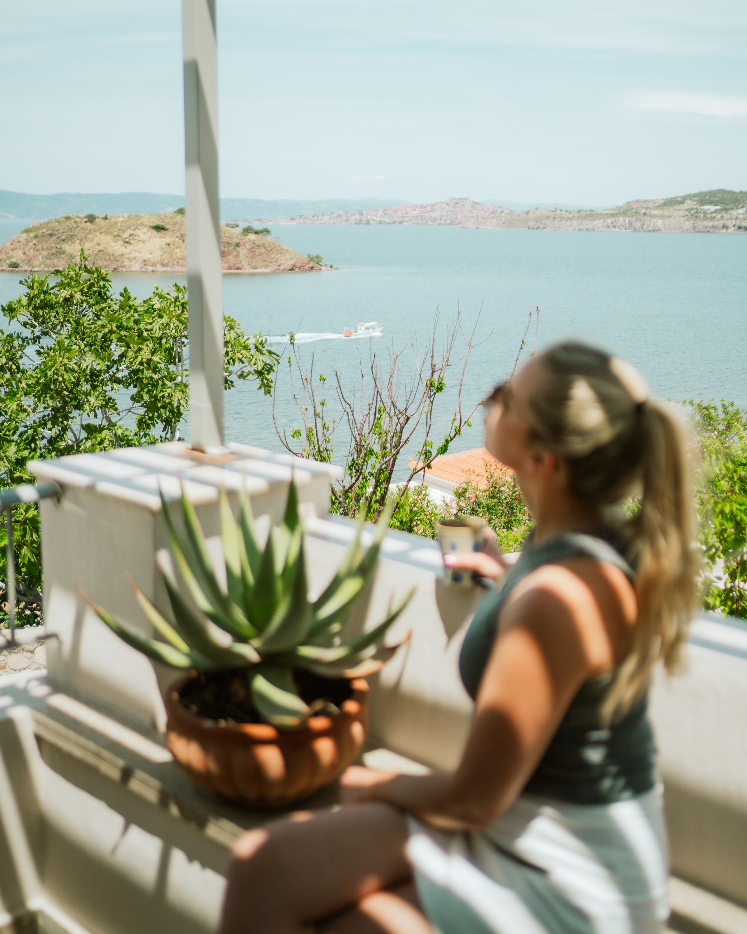 A person sitting on a balcony overlooking a body of water with a boat in the distance.