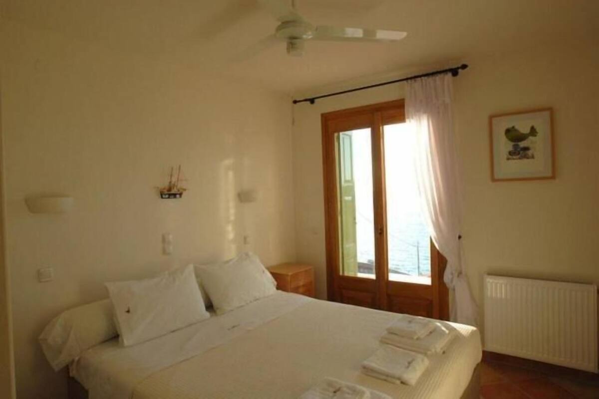 A bedroom with a bed, a nightstand, a window with curtains, a ceiling fan, and a framed picture on the wall.