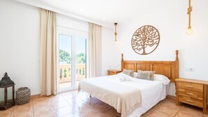 Een slaapkamer met een bed, houten nachtkastjes, een ronde decoratie aan de muur en uitzicht door de glazen deur.
