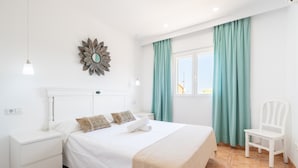 Een keurig opgemaakt slaapkamer met een bed, nachtkastjes, een stoel, een decoratieve spiegel en een raam met gordijnen.