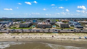 A coastal cityscape with a beachfront hotel, a large parking lot, and a clear blue sky. - Shell-Abration-Like a Beach Fiesta (Galveston)