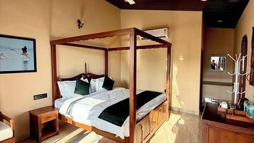 Una cama con dosel, un ventilador de techo, una mesita de noche pequeña, una silla y un aparador de madera con espejo.