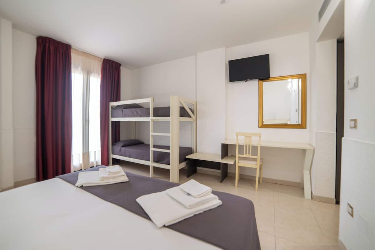 A hotel room with bunk beds, a desk, a chair, a flat-screen TV, and a mirror.