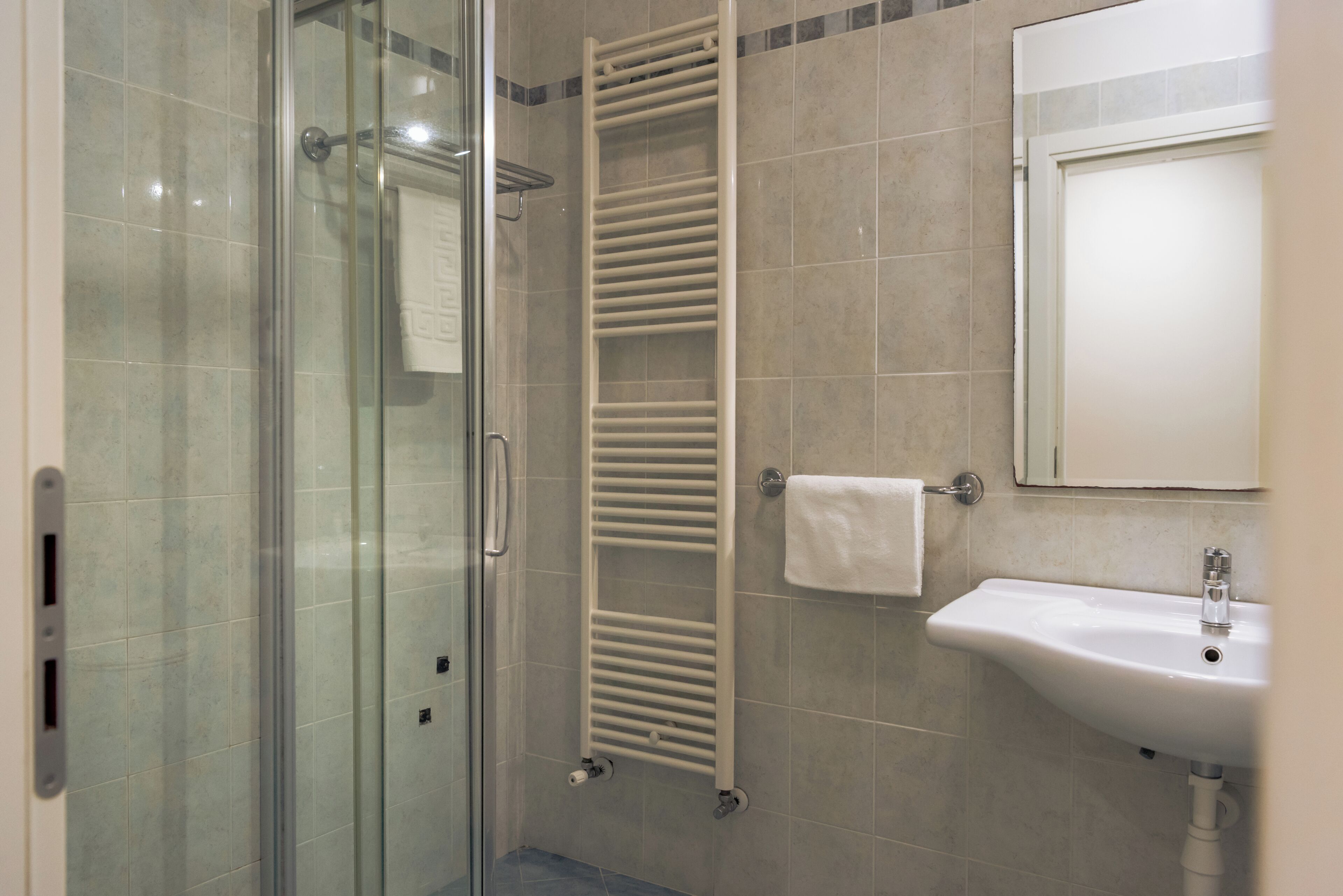 Un bany amb una cabina de dutxa de vidre, un penjador de tovalloles i un lavabo.