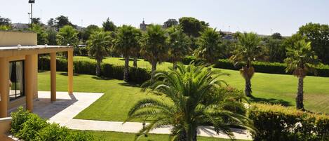 Un jardín bien cuidado con palmeras, cielo despejado y un edificio moderno con un patio cubierto.