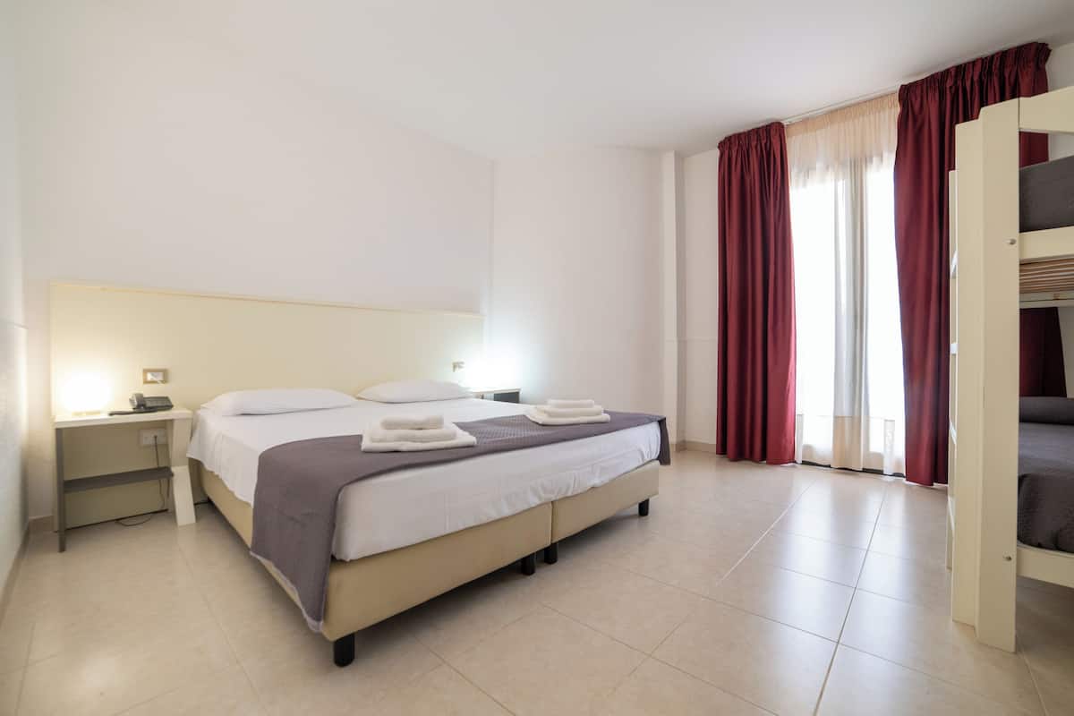 A hotel room with a bed, bedside table, and a window with curtains.