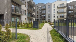 Un edificio de apartamentos moderno con balcones, un sendero pavimentado y un letrero que indica la dirección.