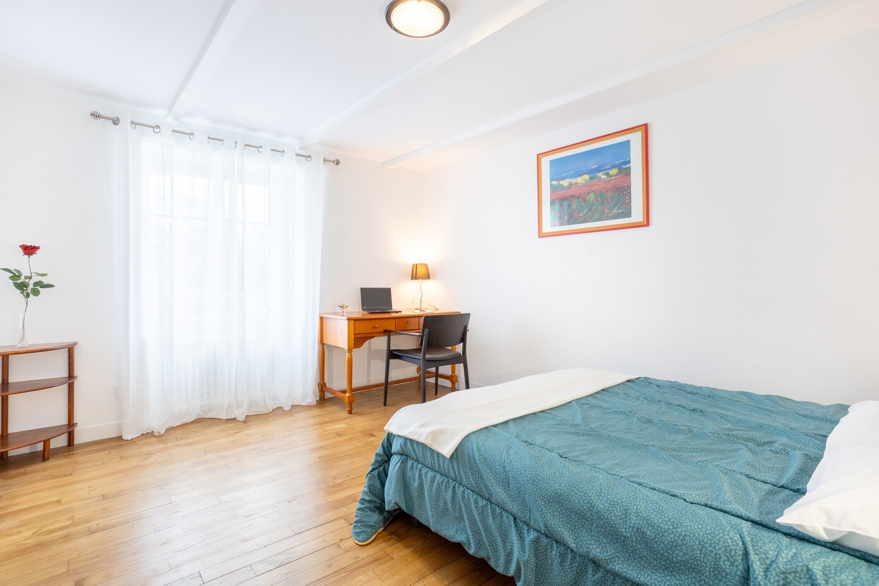 Une chambre à coucher avec un lit, un bureau, une chaise, une lampe et un tableau au mur.