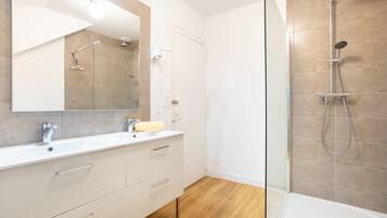 Une salle de bain moderne avec une douche à parois de verre, un meuble-lavabo blanc avec un miroir et un plancher en bois.