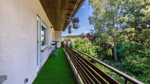Un balcon avec un revêtement de gazon synthétique, une rambarde en bois et des jardinières suspendues.