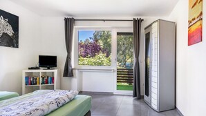 Une chambre à coucher comprenant un lit, un téléviseur, une bibliothèque, une porte coulissante donnant sur un balcon et une armoire.
