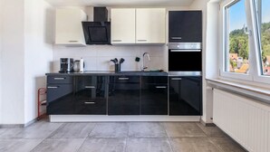 Une cuisine moderne avec des meubles de rangement noirs et blancs, une hotte de cuisine en acier inoxydable et une fenêtre donnant sur des immeubles.