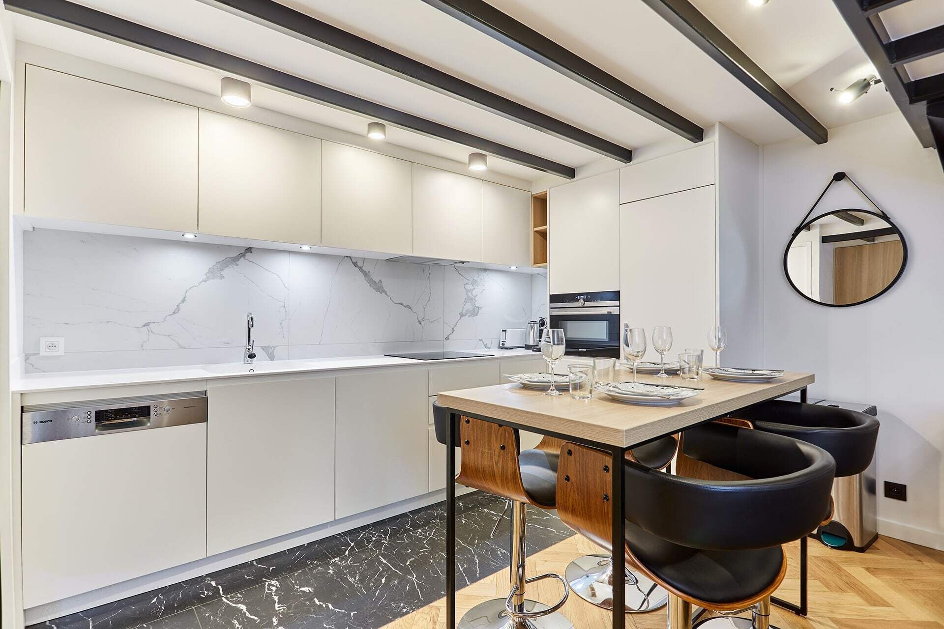 A modern kitchen with white cabinets, a marble backsplash, and a dining area with a wooden table and black chairs.