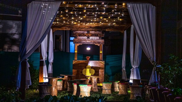 Un área de estar al aire libre con una estructura de madera, cortinas colgantes y luces de adorno.