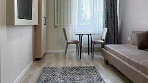 Ein modernes Hotelzimmer mit einem an der Wand befestigten Flachbildfernseher, einem Essbereich mit Tisch und Stühlen, einem Sofa und einem gemusterten Teppich.