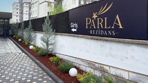 Ein modernes Mehrfamilienhaus mit einem Schild für "PARLA - REZIDANS" und einem Pfeil, der nach links weist.
